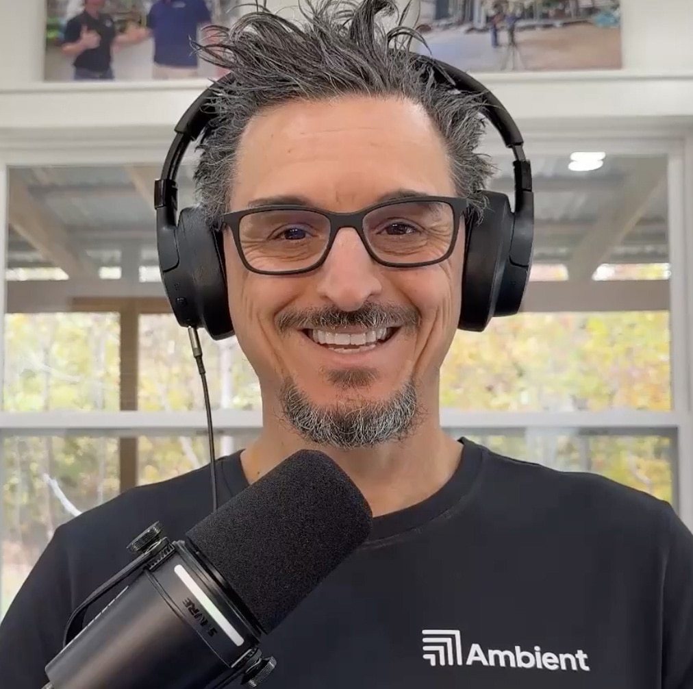 A photo of Tony Mormino smiling, wearing headphones and sitting behind a microphone.